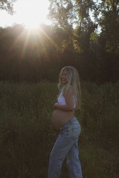 a pregnant woman standing in the grass with her belly exposed and sun shining behind her