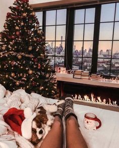 a woman laying in bed next to a christmas tree with her feet on the pillow