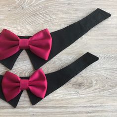 two black and pink bow ties sitting on top of a wooden table next to each other