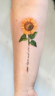 a sunflower tattoo on the arm with words written in cursive writing below it