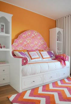 a bedroom with orange walls, white furniture and pink rugs on the hardwood floor