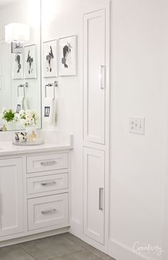 a white bathroom with two sinks and pictures on the wall