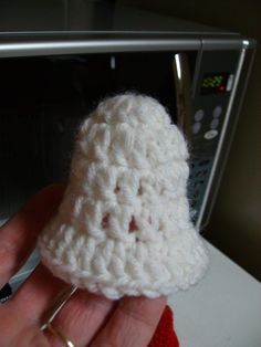 a hand holding a small white crocheted object in front of a microwave