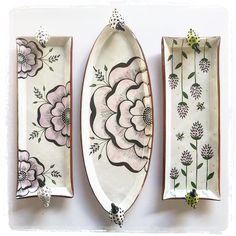 three plates with flowers painted on them are sitting next to each other in front of a white wall