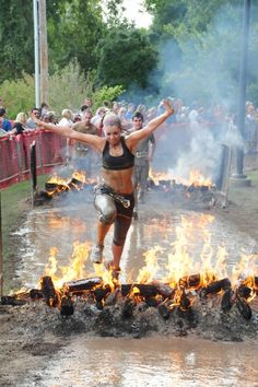 a woman jumping in the air over a fire pit with her arms outstretched and legs spread wide