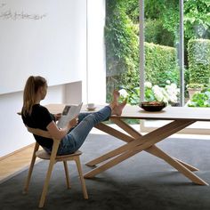 a woman is sitting at a table with a laptop in her lap and looking out the window