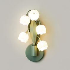 a green vase with five white flowers on it and a light attached to the wall