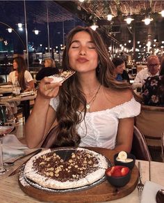 a woman sitting at a table in front of a pie with toppings on it