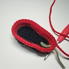 a crocheted red and black object on a white surface next to a pair of scissors