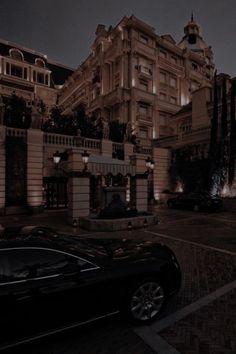 a black car parked in front of a tall building at night with street lights on