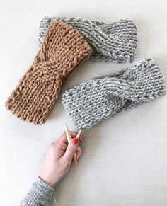 two knitted mittens and a hand holding knitting needles on a white tablecloth