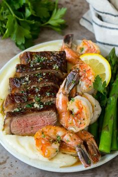 steak, shrimp and asparagus on a plate with lemon wedged garnish