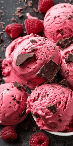 raspberry ice cream with chocolate chunks on a black surface surrounded by raspberries