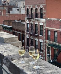 two glasses of wine sitting on top of a cement ledge in front of a brick building