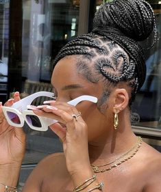 a woman wearing white sunglasses and braids holding up her eyeglasses to her face