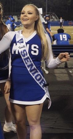 a cheerleader is standing on the sidelines with her hand in her pocket and smiling