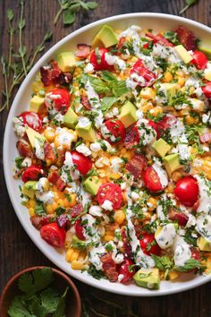 a salad with tomatoes, corn and avocado in a white bowl on a wooden table