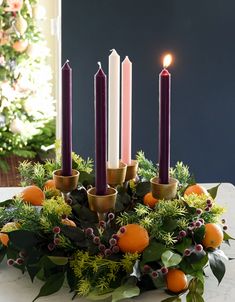 an arrangement of candles on a table with oranges and greenery in the center