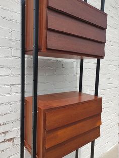 a wooden shelf next to a white brick wall with black metal bars on the bottom