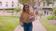 a woman walking down a sidewalk with a book in her hand and people behind her