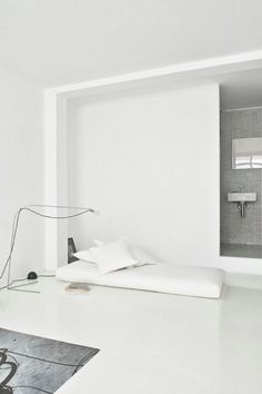 a white room with a bed, lamp and pictures on the wall in it's corner