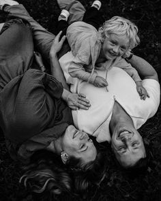 a black and white photo of three people laying on the ground with one holding a child