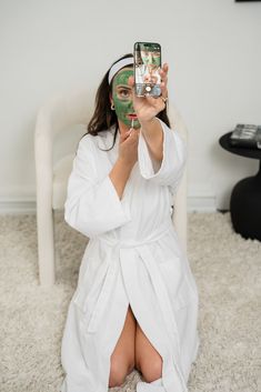 a woman in a bathrobe taking a selfie with her cell phone while sitting on the floor