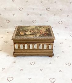 an antique wooden box with shells in it on a white tableclothed background that has hearts drawn all over the surface