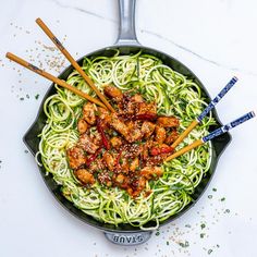 a skillet filled with noodles and chicken on top of a white table next to chopsticks