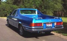 an old blue car is parked on the side of the road in front of some trees