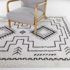 a gray chair sitting on top of a white rug next to a wooden arm chair