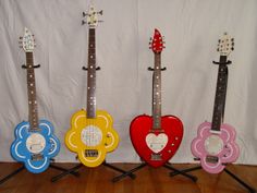 four colorful guitars are lined up in front of a white backdrop with flowers on them