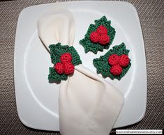 two napkins with crocheted holly decorations on them sitting on a white plate