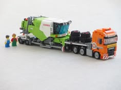 a toy truck with two people standing next to it on a white surface and one person is looking at the back of the truck