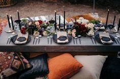 the table is set with candles, plates and flowers in black vases on it