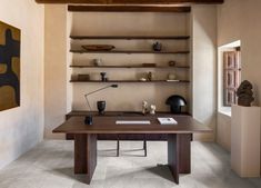 a wooden desk sitting under a window next to a shelf filled with vases and books