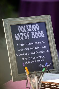 a sign that says polaroid guest book next to pens and pencils on a table