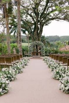 an outdoor ceremony setup with white flowers and greenery at the end of the aisle