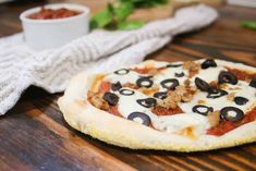 a pizza with olives on it sitting on top of a wooden table