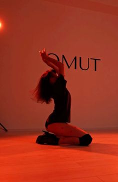 a woman kneeling on the floor in front of a red light with her arms up