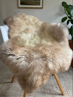 a chair made out of sheepskin with wooden legs on carpeted floor next to potted plant