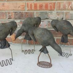 three metal birds sitting on top of each other next to a brick wall and wire