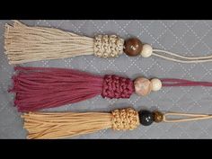 three tassels with beads and rope on a gray tablecloth background, one is red, the other beige