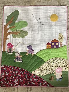 a quilted wall hanging on the side of a brick wall with houses and trees