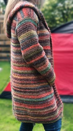 a woman standing in the grass wearing a multicolored cardigan sweater and jeans