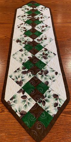 a green and white quilted table runner with pine cones on the top, along with brown trim