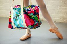 a woman carrying a colorful floral bag with her feet on the ground and wearing ballet shoes