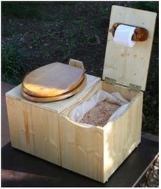 an open toilet sitting on top of a wooden box next to a trash can and grass