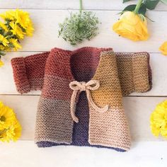 two crocheted sweaters sitting next to yellow flowers