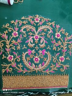 a piece of cloth that has been embroidered with gold and pink flowers on it, sitting next to some thread